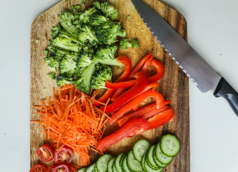 Chopping board with cut up broccoli, peppers, carrots, cucumbers, and cherry tomatoes