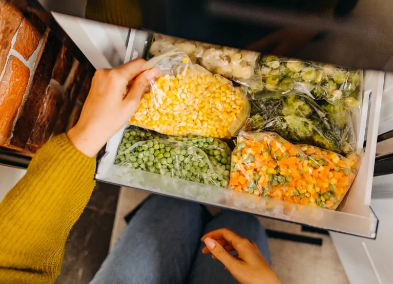 Open freezer with frozen corn, peas, carrots, and cruciferous vegetables