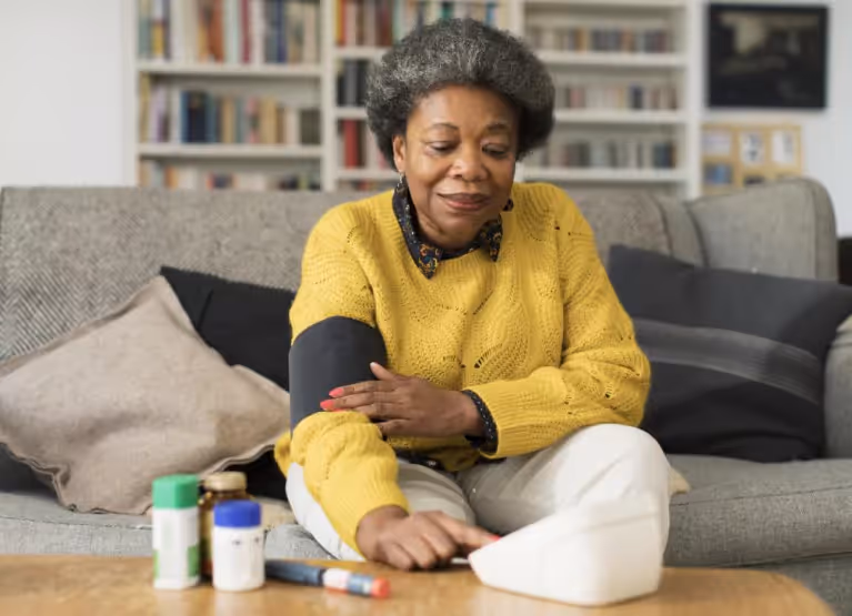 Woman in yellow sweater measuring blood pressure while sitting on couch