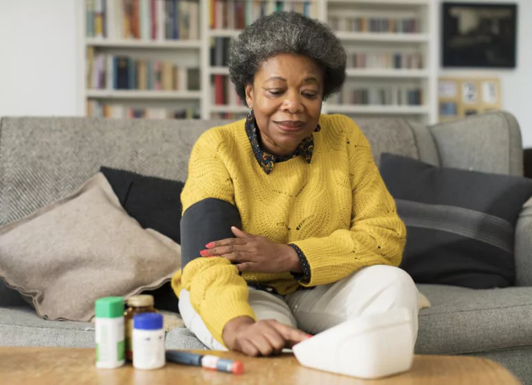 Woman in yellow sweater measuring blood pressure while sitting on couch