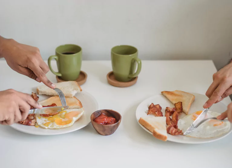 two people cutting into a plate of breakfast food