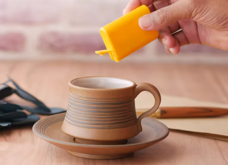 Person pouring splenda into coffee cup
