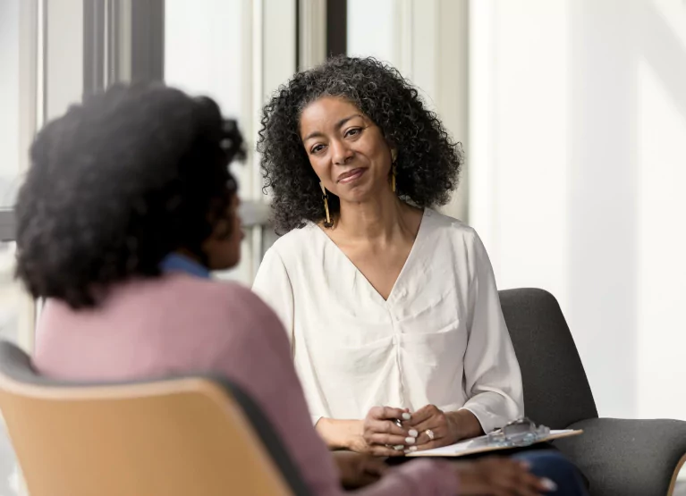 Two women sitting in front of a table, one offering the other support