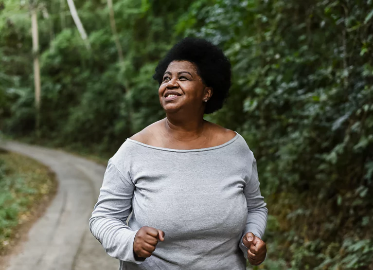 An older woman with short black hair wearing a long grey top and running outdoors