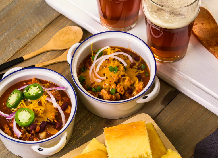 Glasses of beer beside bowls of chilli with cheese