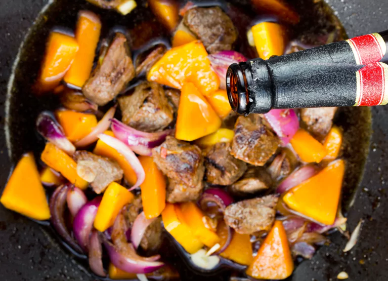 Pouring beer onto root vegetables and stew beef