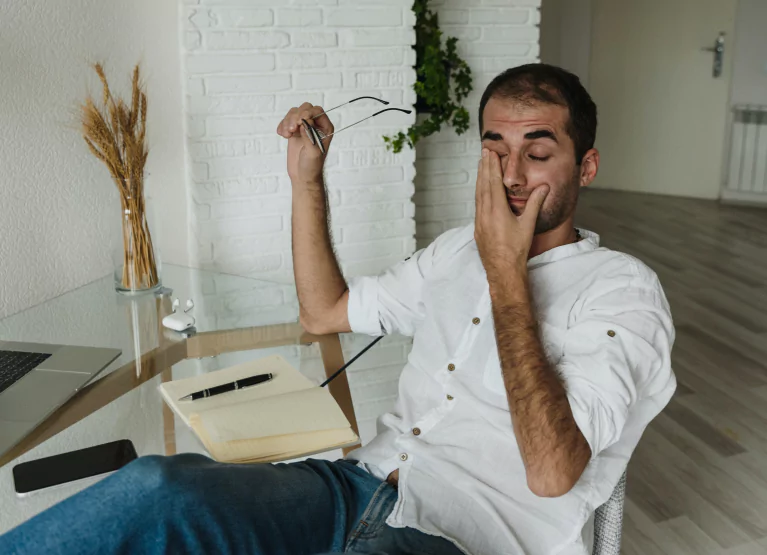 a boy rubbing his eyes and sitting at a desk