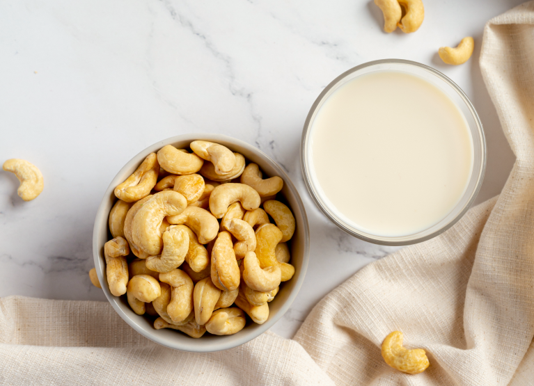 Bowl of cashews beside glass of cashew milk