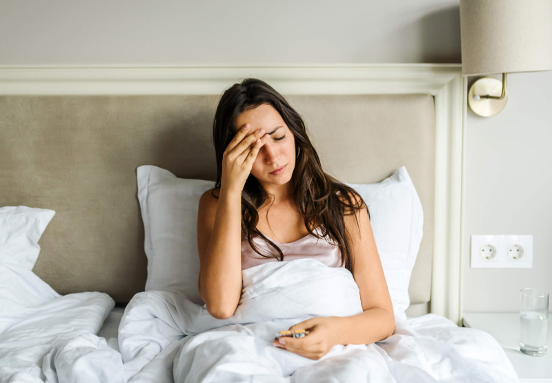 Woman sitting up in bed and holding her head