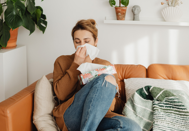 Woman blowing nose while sitting on couch