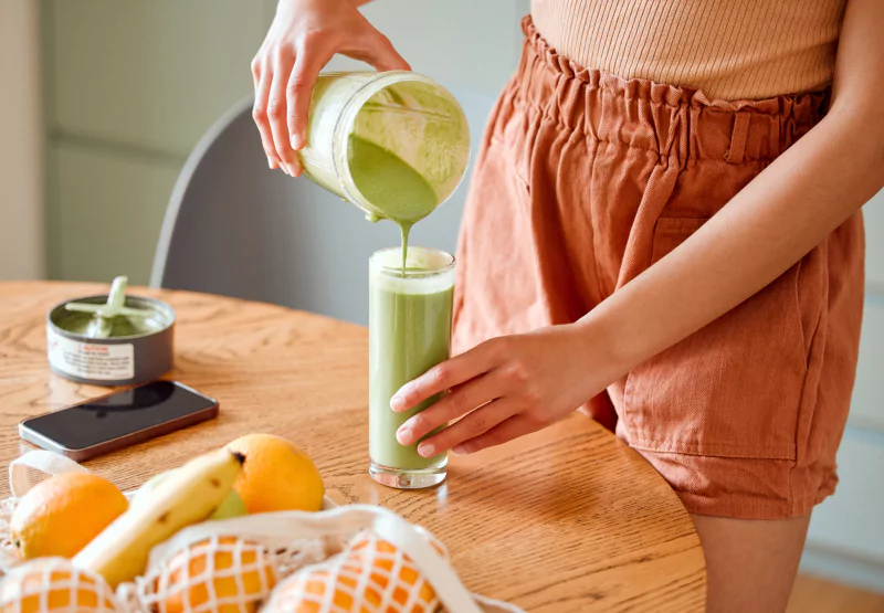 Person pouring green smoothie into glass