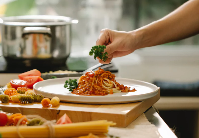 A closeup of a hand adding fresh parsley to a plate of spaghetti