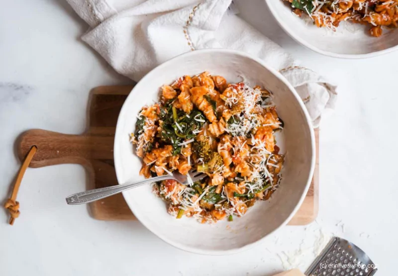 Spinach and parmesan pasta in a white bowl on a wooden chopping board