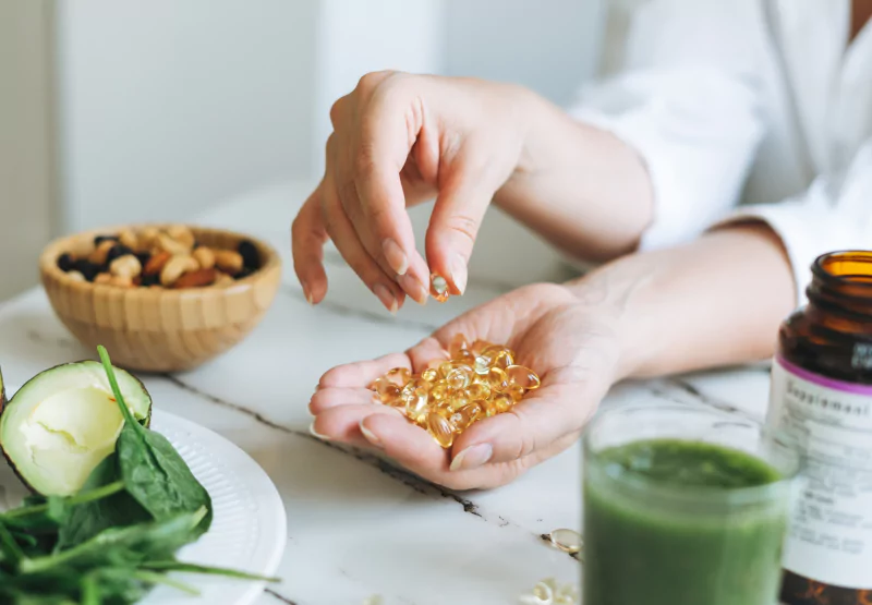 A closeup of hands holding loose supplement pills with greens and nuts in the backgroundu