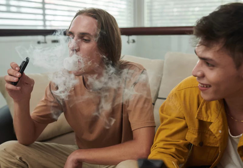 two boys sitting on a couch while using a vape