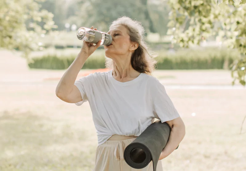 a woman drinking water and holding a yoga mat