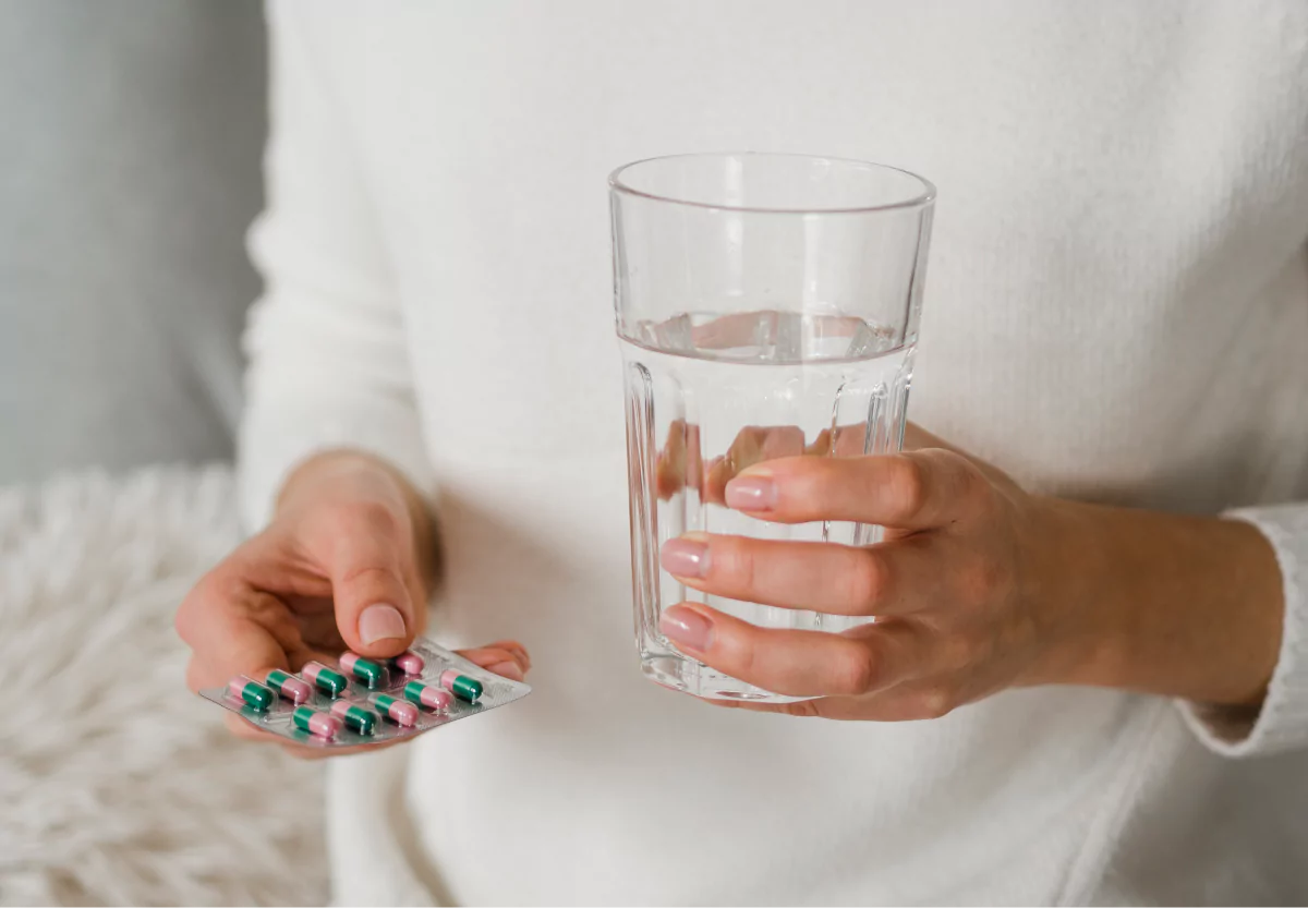 someone holding a glass of water and probiotic supplements