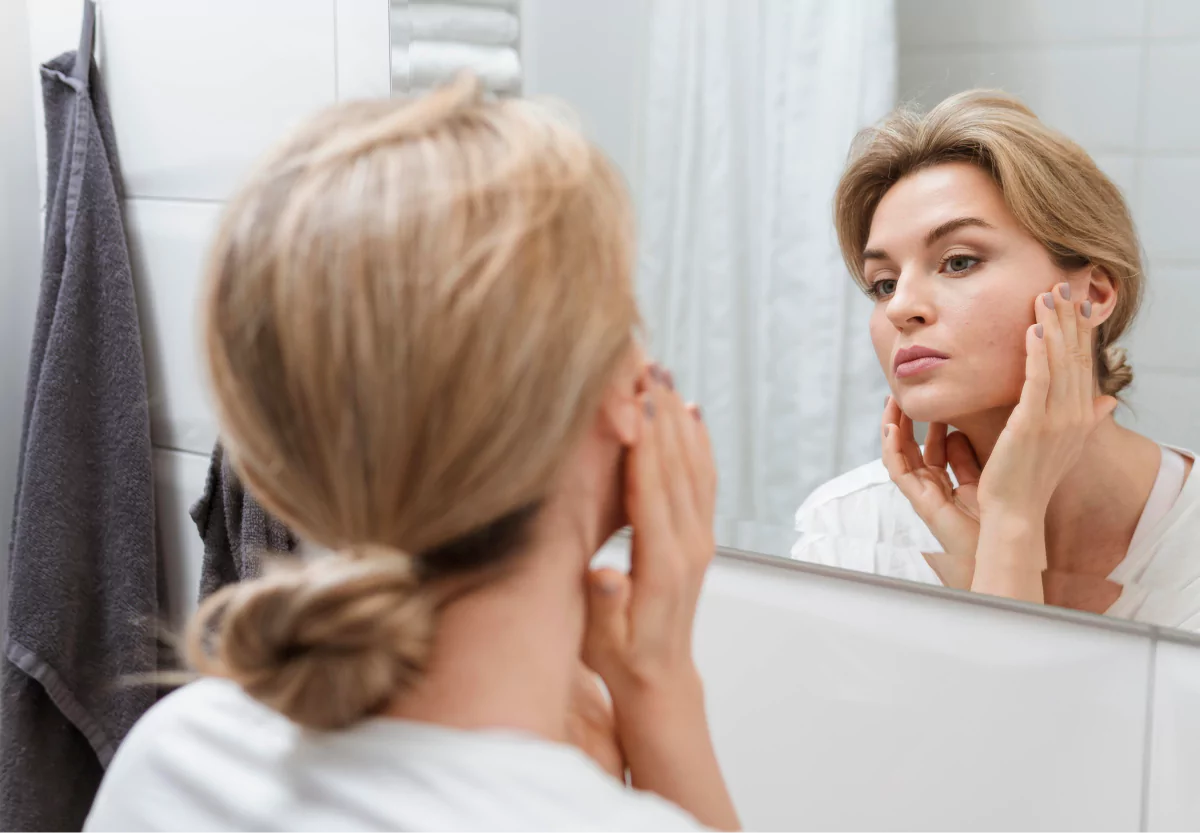 a womanlooking at her skin in the mirror