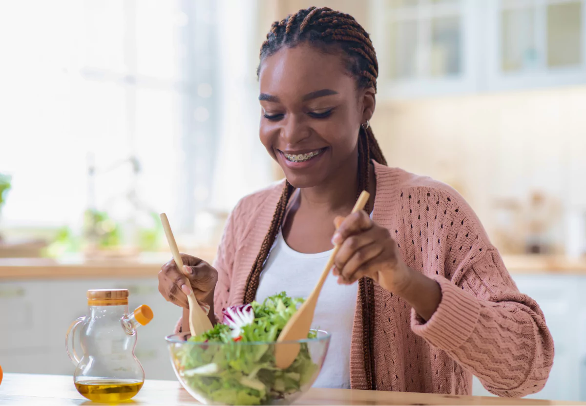 a woman mixing a bowl of salad greens with olive oil