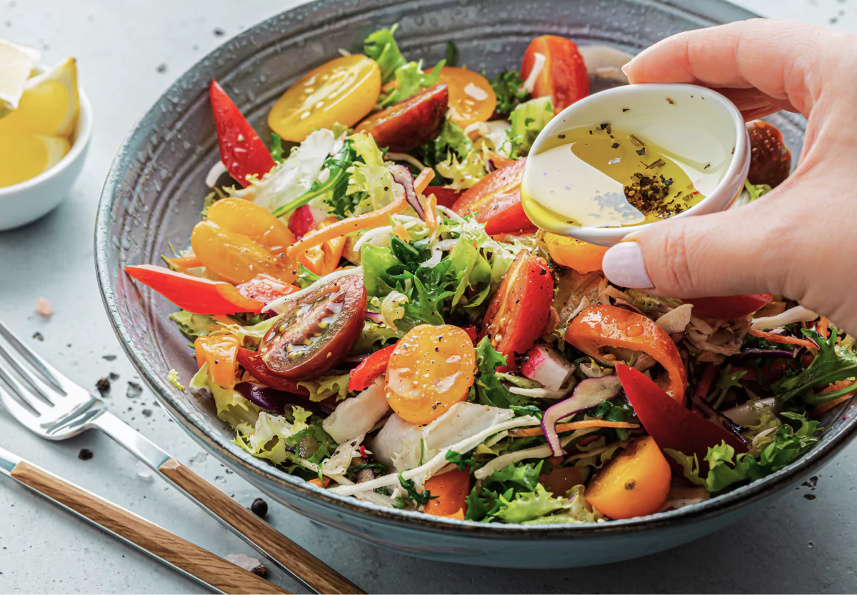 a colorful bowl of  salad with olive oil, tomatoes, greens, lemon