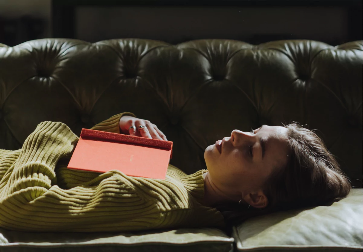 a woman holding a book while laying on a couch