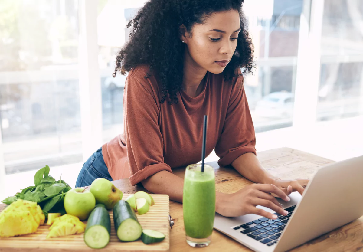 a woman drinking a green juice and working at the computer