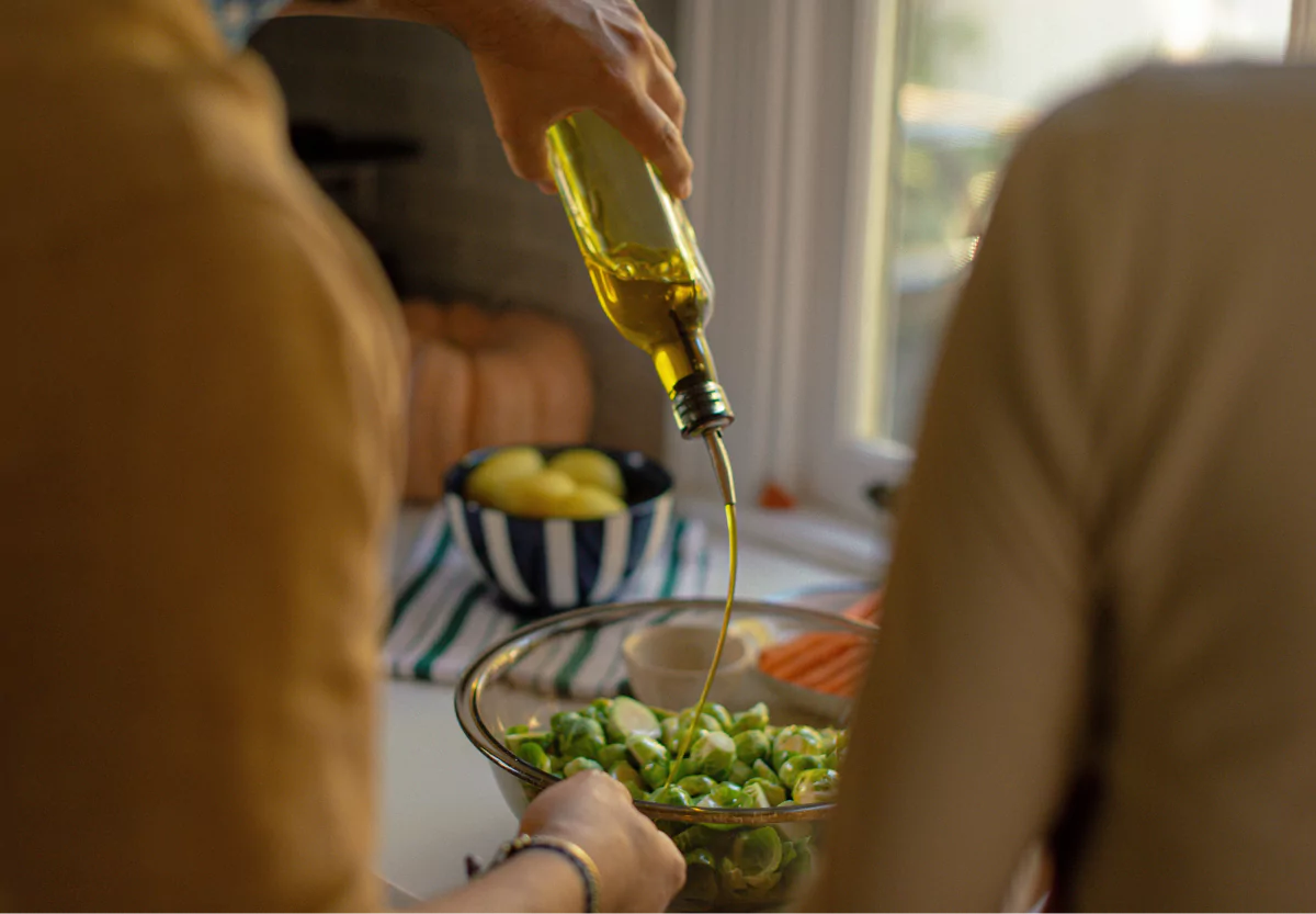 someone pouring olive oil on veggies