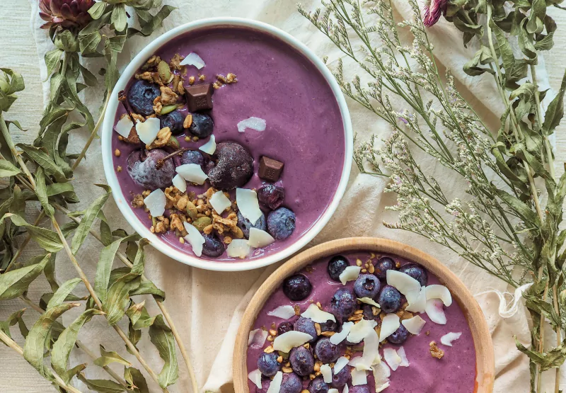 Two white bowls with purple blended yogurt, berries and nuts in an acai bowl