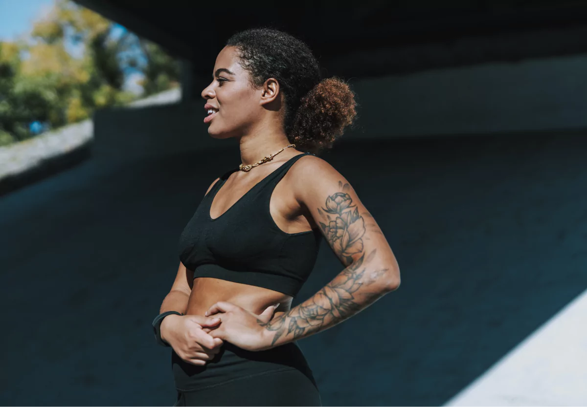 A woman in black workout gear, with hand on hips exercising outdoors