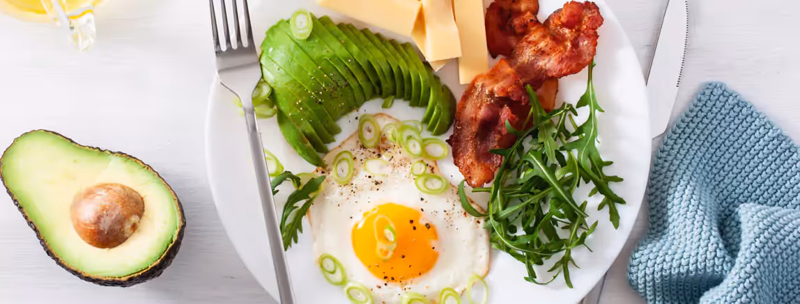 a plate of a fried egg, cut avocado, bacon and cheese