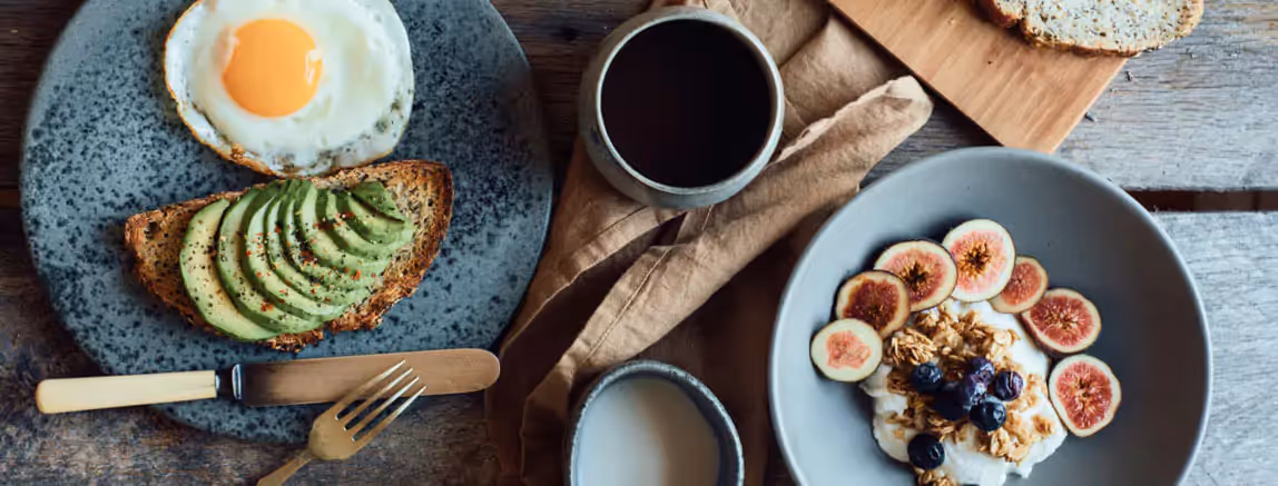 an avocado toast, an egg, a cup of coffee and a bowl of yogurt with berries