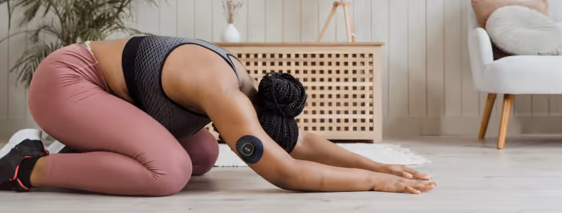 A person doing yoga in pink tights and a black top, wearing the Nutrisense CGM on their arm