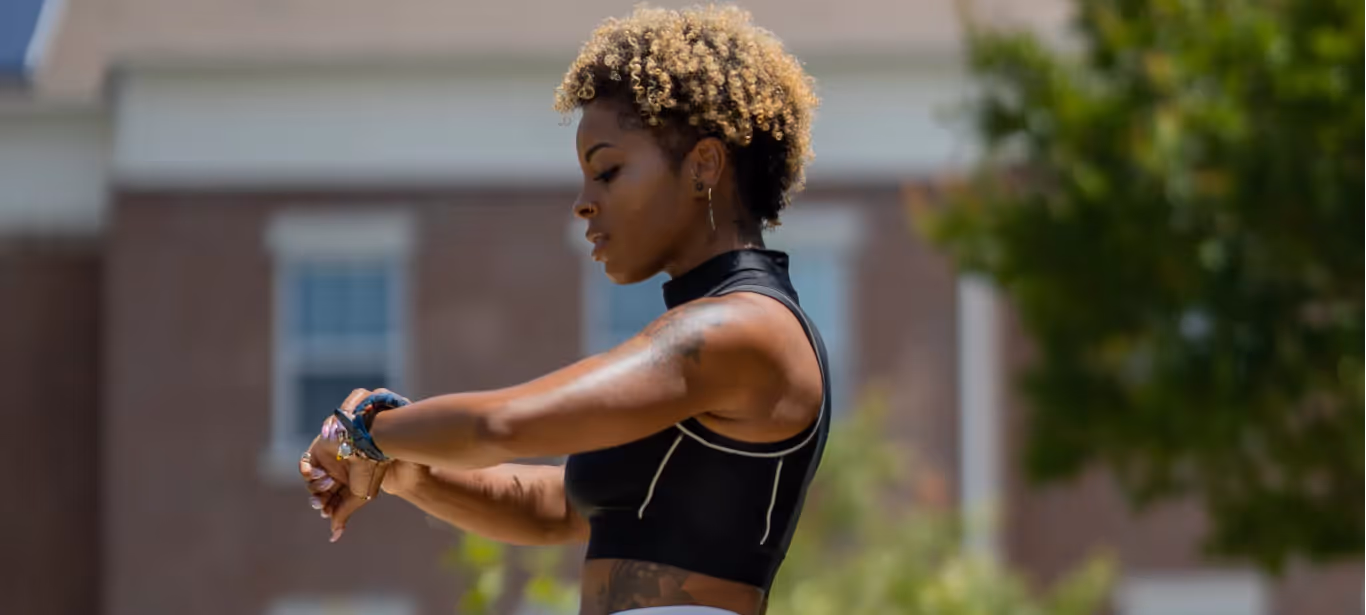A woman with short hair in workout gear, checking her watch outdoors