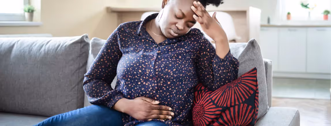 a person sitting on a sofa and holding their stomach in pain