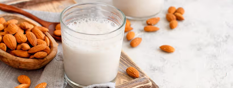 A spoonful of almonds next to a glass of almond milk