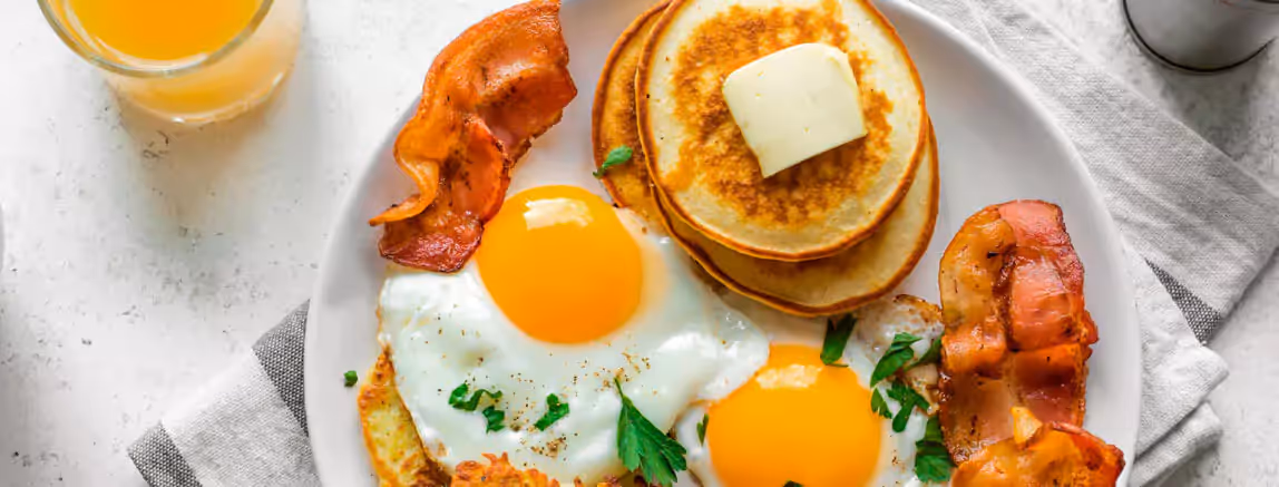 eggs, bacon and pancakes on a plate and a glass of orange juice