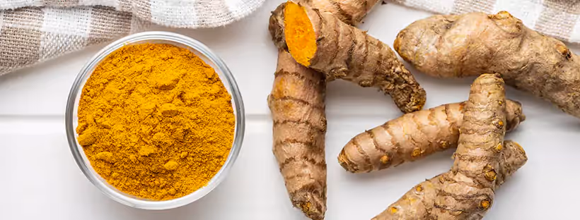 A bowl of turmeric powder near a group of fresh turmeric root