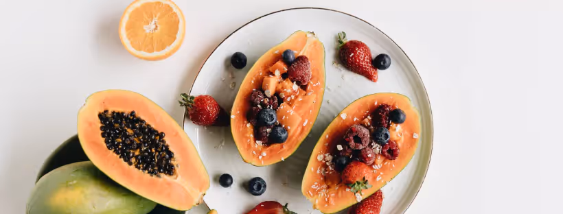 A plate with halves of a papaya, topped with berries and sugar