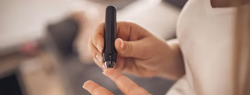 A close-up of someone's hands using a fingerstick to check blood sugar levels