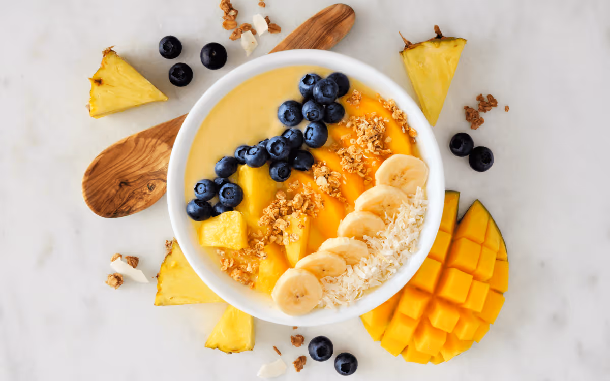A bowl of yogurt and fruits including blueberries, mangoes, bananas, and pineapple topped with granola