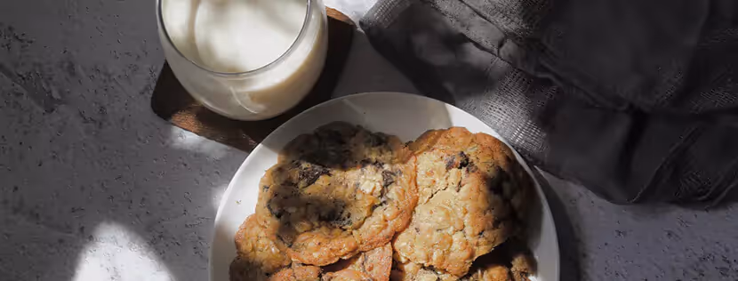 A plate of chocolate chip cookies next to a glass of milk
