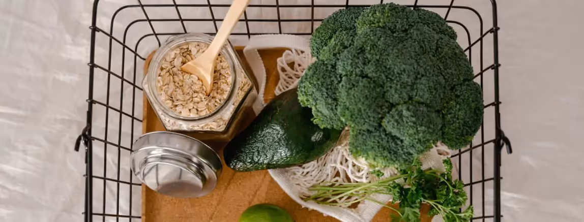 a grocery basket of broccoli, an avocado and a jar of oat flakes