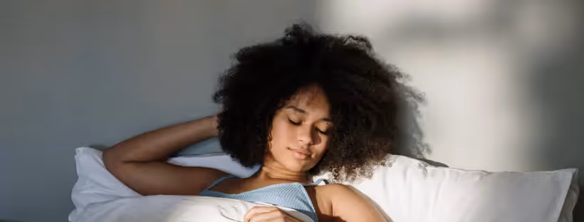 A woman with curly black hair asleep against a white pillow
