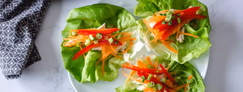 A plate with three lettuce wraps garnished with grated carrots, red peppers and green onions