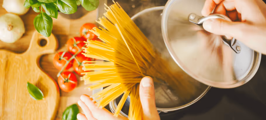 A closeup of hands holding the lid to a pot of raw pasta