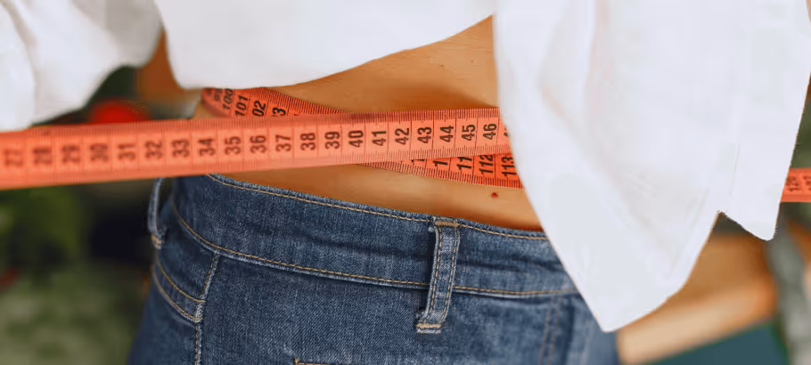 A closeup of someone checking their waist size with a measuring tape