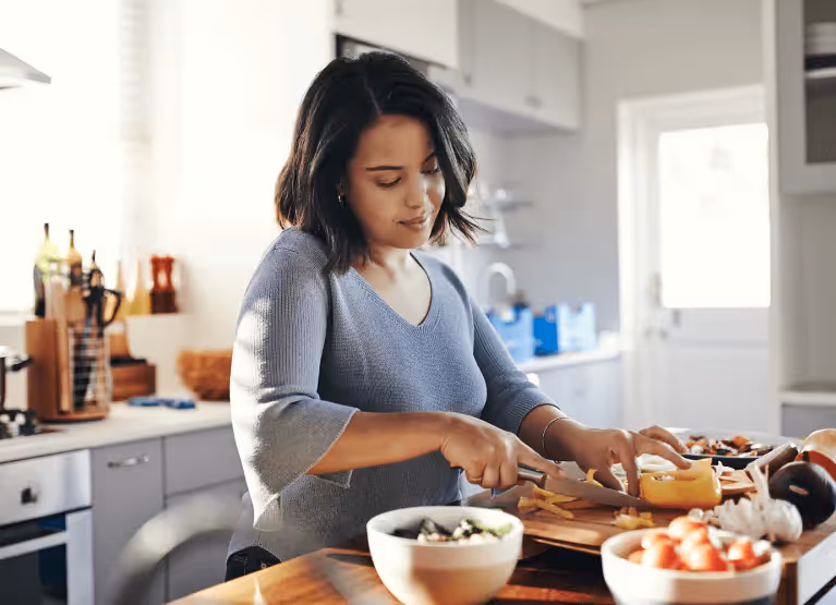 A woman with mid-length black hair chopping vegetables in a kitchen.