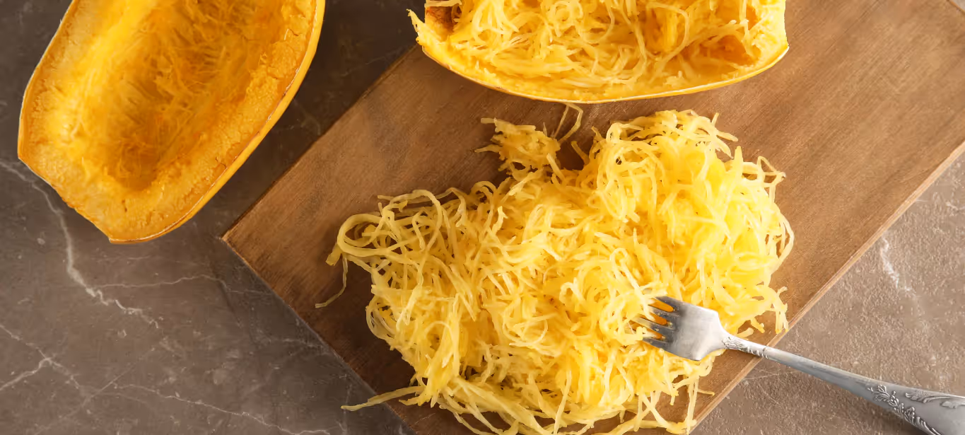 An image of two spaghetti squash halves cut open, with spaghetti squash flesh on a wooden chopping block with a fork sticking through it