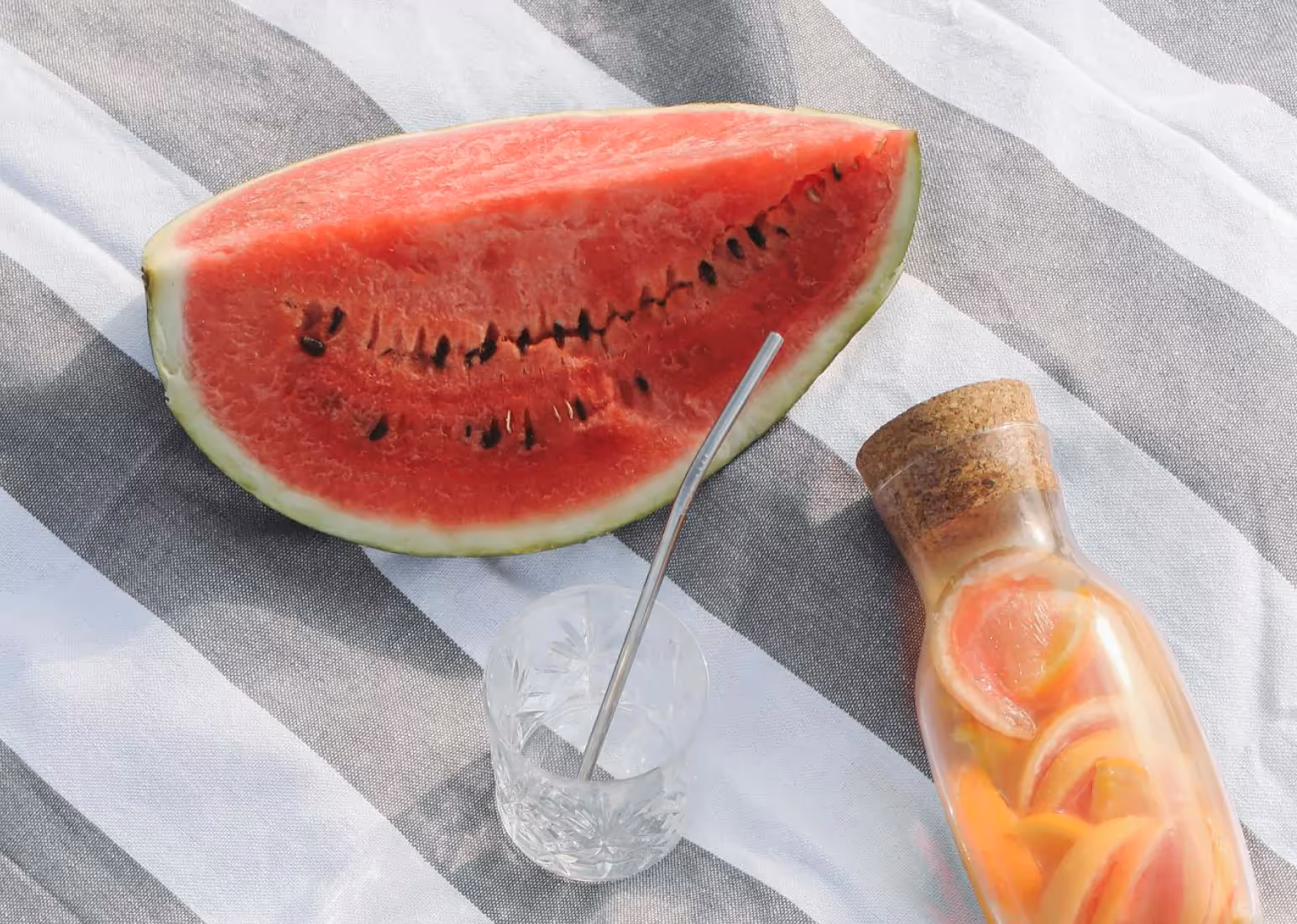 a slice of watermelon on a white and grey backdrop accompanied by a glass and spoon