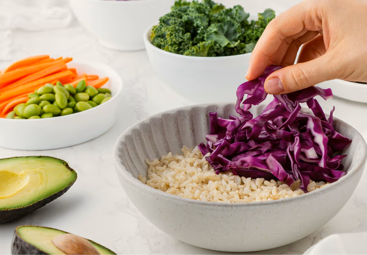 A table with a variety of white bowls filled with colorful vegetables including carrots, purple cabbage, Kale and edamame beans